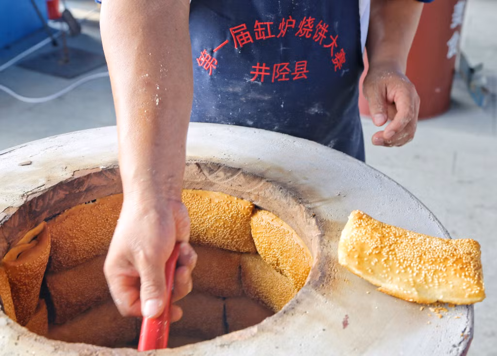 2024年8月24日，在河北石家庄市一缸炉烧饼大赛上，缸炉烧饼参赛者正在将烧饼出炉。 Ngày 24 tháng 8 năm 2024, tại cuộc thi bánh nướng lò gốm ở Thạch Gia Trang, Hà Bắc, các thí sinh đang đưa bánh nướng ra khỏi lò.