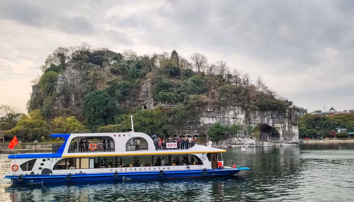 游客乘游船观赏桂林市城徽象鼻山 Khách du lịch đi thuyền ngắm núi Mũi Voi – biểu tượng của thành phố Quế Lâm