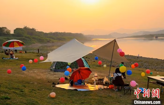 依山傍水的露营地，布满了汽车和帐篷。 Khu cắm trại “kề sông tựa núi” chật kín xe hơi và lều cắm trại.