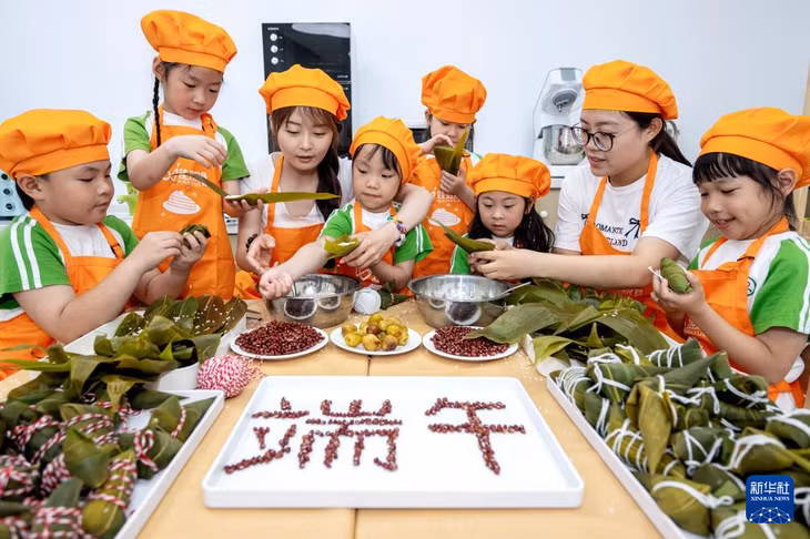 在浙江省湖州市长兴县泗安镇中心幼儿园，孩子们体验包粽子。 Các em nhỏ trải nghiệm gói bánh chưng tại Trường Mầm non Trung Tâm thị trấn Tứ An, huyện Trường Hưng, thành phố Hồ Châu, tỉnh Chiết Giang.