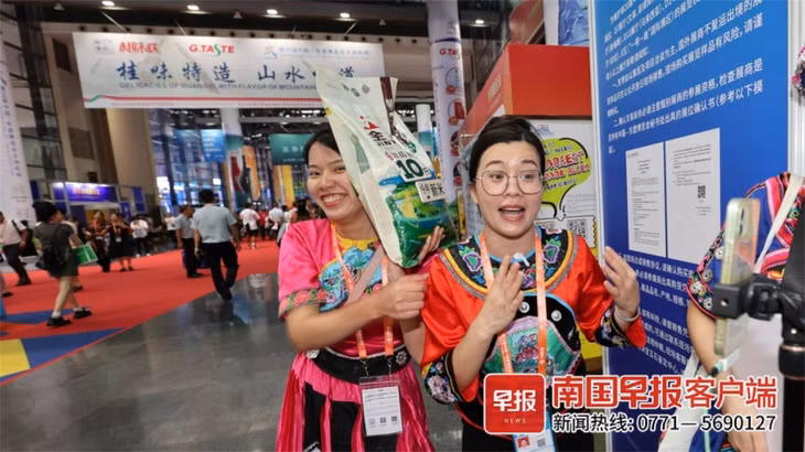 东博会上，身穿少数民族服饰的主播正在直播卖米。游拥军 摄 Tại Hội chợ triển lãm Trung Quốc - ASEAN, các streamer mặc trang phục dân tộc thiểu số đang livestream bán gạo. Ảnh: Du Ung Quân chụp
